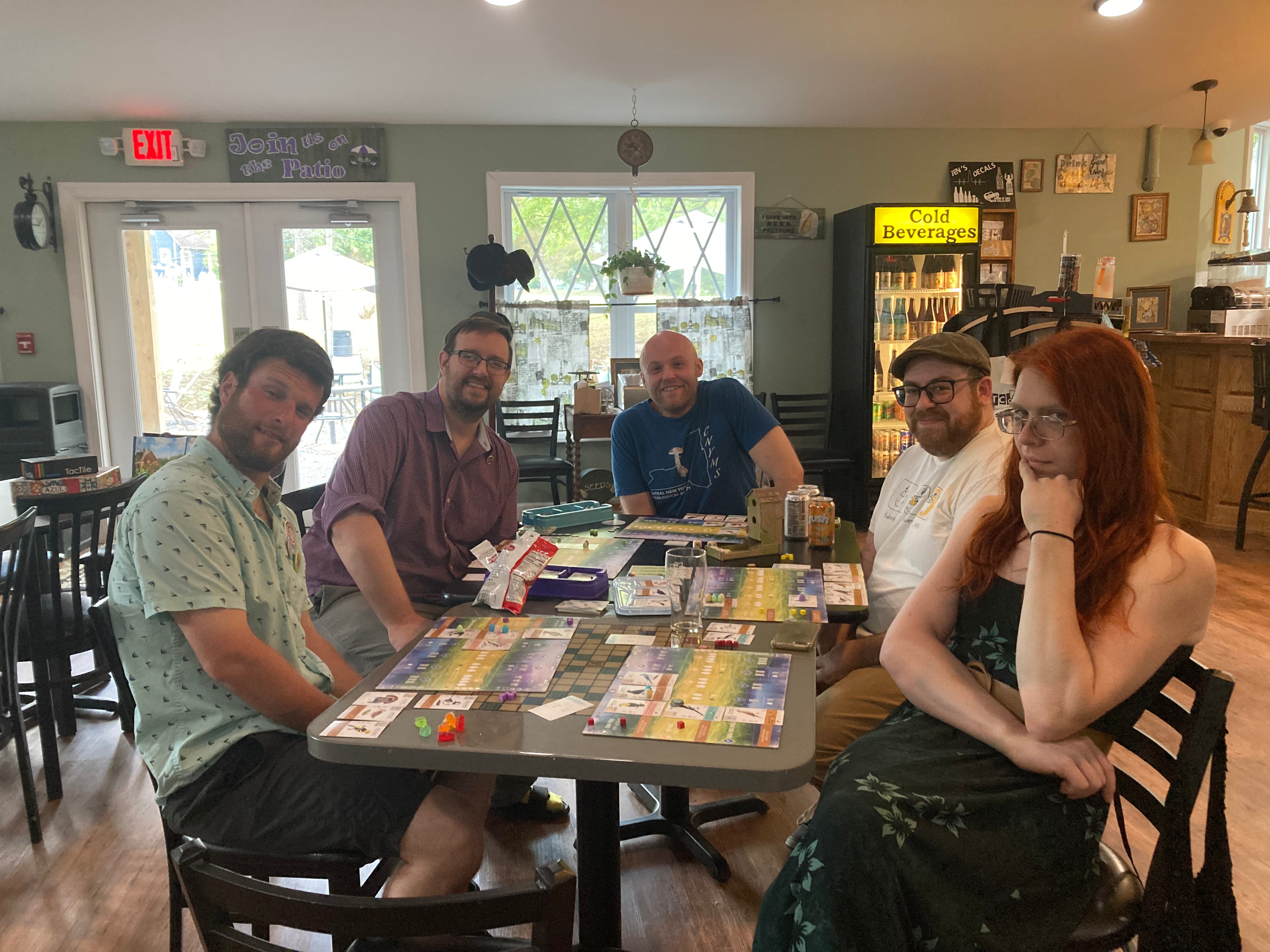 A group of people sitting around a table. They are posing for a photo. A board game is set up on the table.